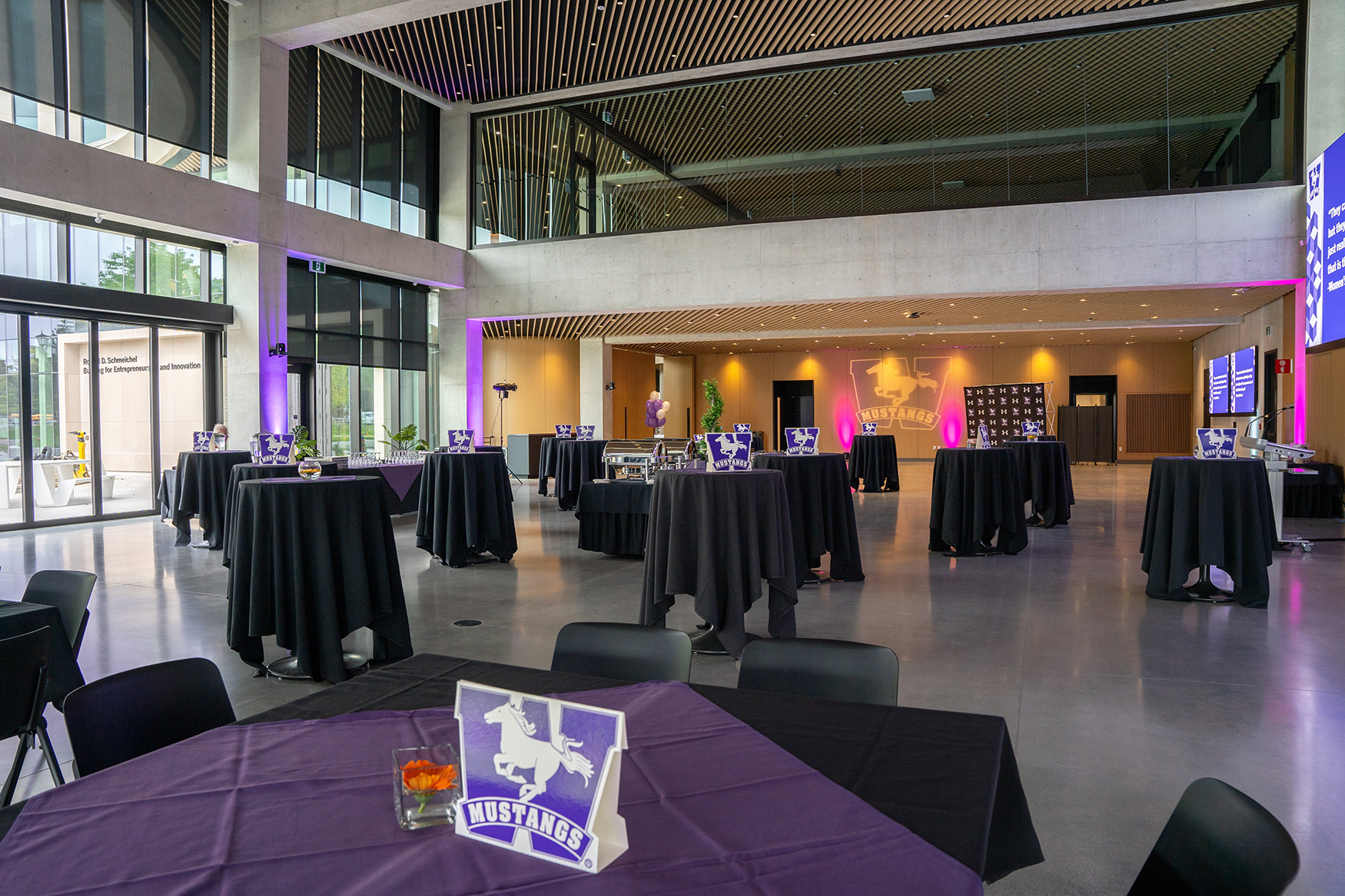 Grand Hall at SEI set up for an event with multiple rectangular tables covered in white cloths, black chairs, and large floor-to-ceiling windows allowing natural light